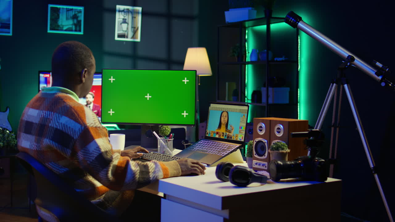 Man working at desk with green screen computer and telescope