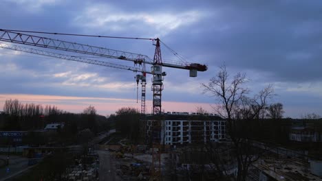 Sie-Fliegen-Hoch-Und-Zeigen-Einen-Panoramablick-Auf-Im-Bau-Befindliche-Wohngebäude-Mit-Kränen-Vor-Einem-Bewölkten-Sonnenuntergangshimmel