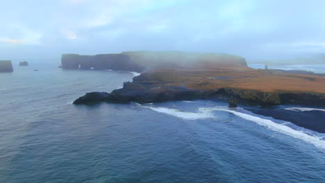 drone cinematográfico aéreo panorámica desde el océano impresionante amanecer temprano en invierno en la playa de arena negra apóstoles fuego y hielo océano junto a dyhrolaey faro reynisfjara islandia