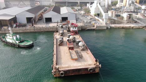 barge loaded with concrete mixer trucks pulled to port by a tugboat in hong kong bay, aerial view