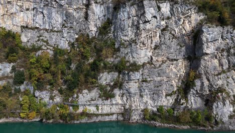 Disparo-Ascendente-De-Un-Dron-De-Una-Empinada-Pared-De-Acantilado-Y-El-Azul-Lago-Suizo-Walensee-Walen-Con-árboles