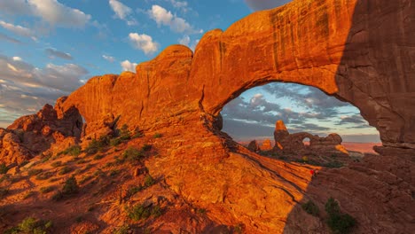 lapso de tiempo dorado del amanecer con luz que se transmite en formaciones geológicas de arco únicas y nubes que fluyen en las ventanas y el arco de la torre en el parque nacional de los arcos, utah, estados unidos