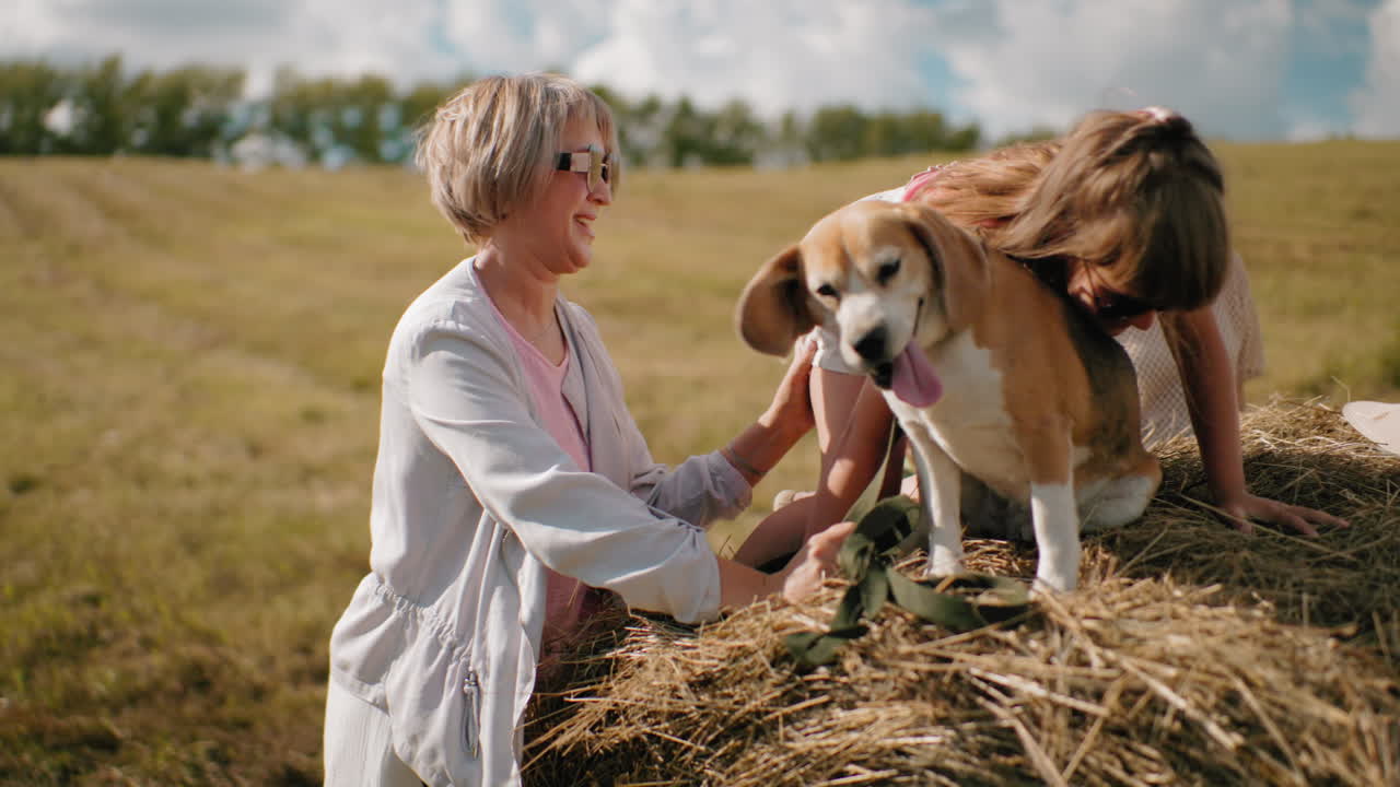 어린 소녀는 줄을 고 개와 함께 건조한 에 올라, 혀를 꺼내, 여자가 아이를 도와주는 동안, 다른 여자는 빛의 시골에서 근처에 서 있으며, 굴곡 된 과 멀리 나무가 있습니다.