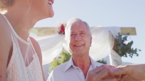 Caucasian-bride-and-groom-standing-at-outdoor-altar-with-wedding-officiant-during-ceremony