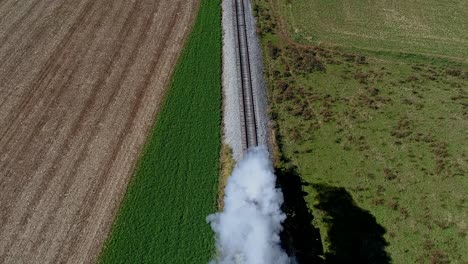 Eine-Luftaufnahme-Direkt-über-Einem-Dampfzug,-Der-Rauch-Und-Dampf-Auf-Die-Drohne-Bläst,-Während-Sie-Durch-Die-Bäume-Fährt