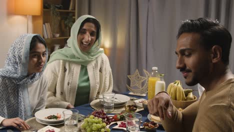 muslim family making video call sitting around table at home eating iftar meal breaking daily fast during ramadan