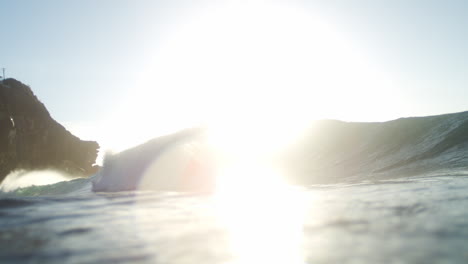 Low sun backlights wave rolling in smooth slow motion