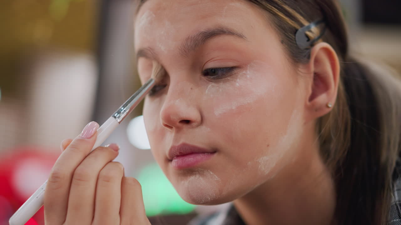 vista de primer plano de una niña joven aplicando polvo en su párpado con un pincel de maquillaje, enfoque detallado en la aplicación del pincel y la rutina de maquilaje ocular, proceso de aplicación de belleza y cosméticos