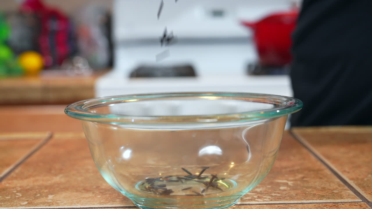 Wilder oder schwarzer Reis wird in Zeitlupe zur Kochvorbereitung in eine Glasschale geschüttet – Seitenansicht.