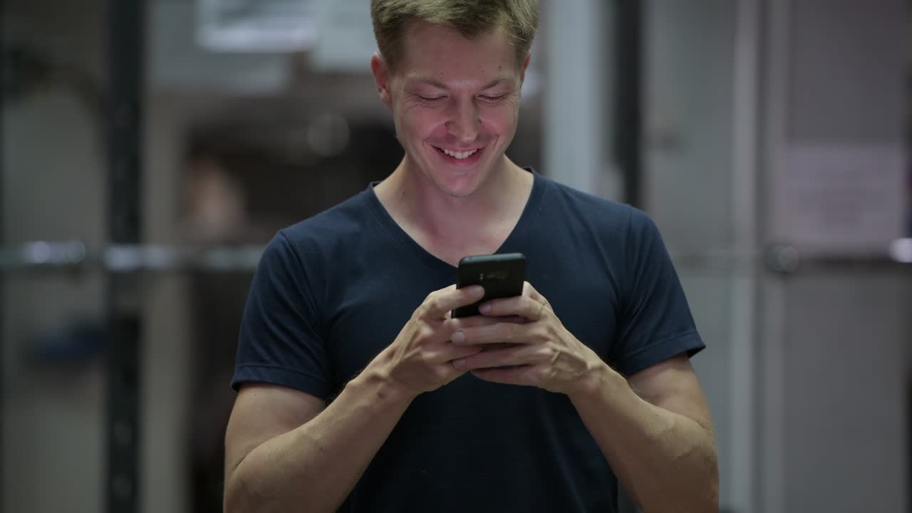 젊은 잘생긴 스칸디나비아 남자가 체육관에서 전화를 사용하고 있습니다.