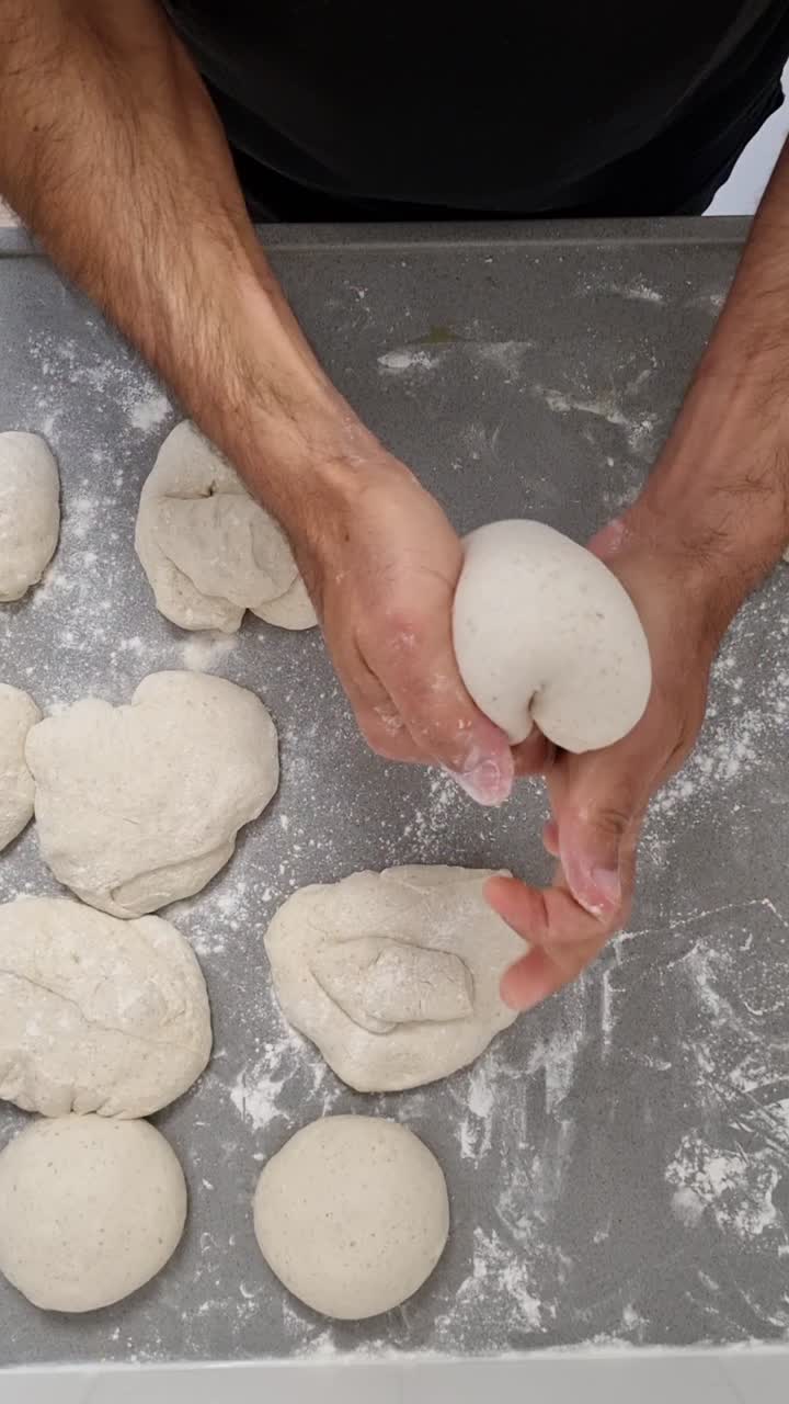 Video verticale dall'alto sulla tecnica di staglio dell'impasto per pizza, che utilizza il metodo della piegatura per modellare l'impasto fermentato a freddo per 48 ore in palline lisce e rotonde.