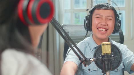 Over Shoulder View Of Asian Kid Girl Host Record Podcast Use Microphone Wear Headphone Interview Happy Boy Guest Conversation For Content In Her Home Studio. Content Creator Concept