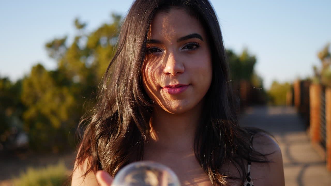 A dreamy hispanic woman with a magic crystal ball staring and smiling in slow motion at sunset