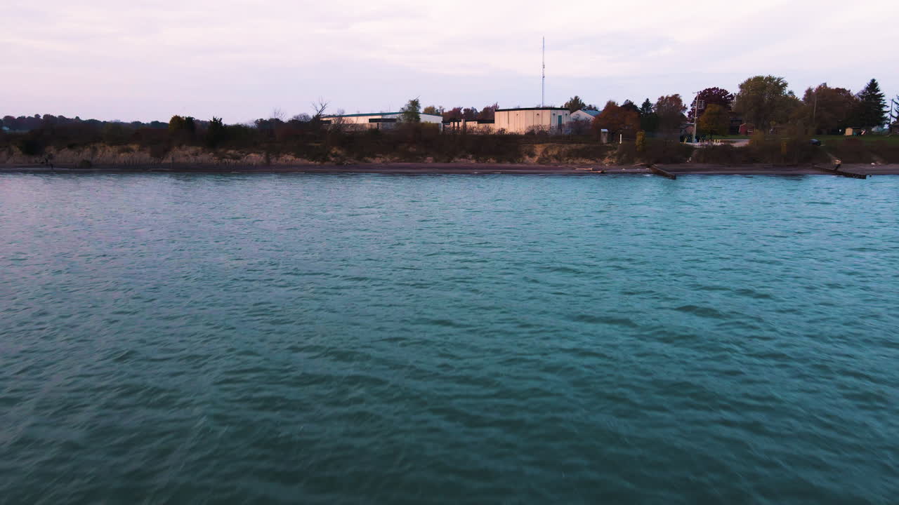 dolly aérea sobre el agua verde turquesa en el borde costero por los edificios de la zona industrial