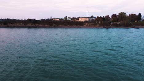 aerial dolly above turquoise green water on coastal edge by industrial zone buildings