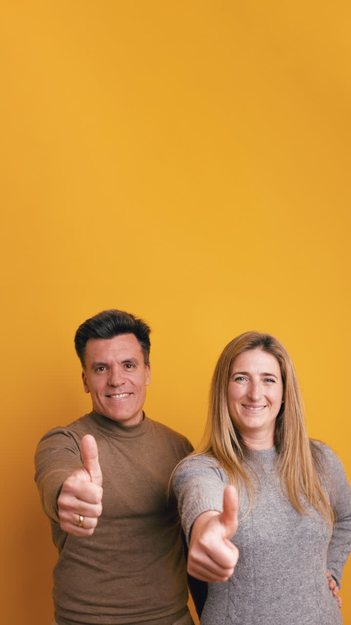Happy Couple Giving Thumbs Up Gesture on Yellow Background