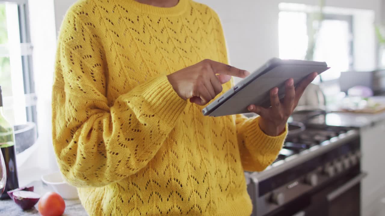 Midsection of african american woman using tablet in kitchen