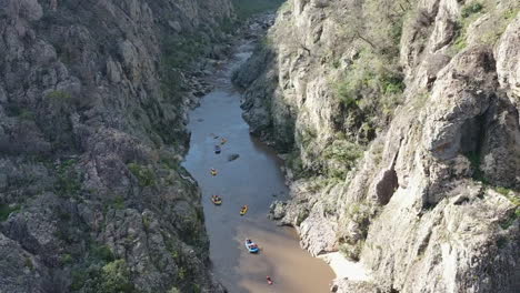 aerial climbs steep rocky cliffs with rafters on snowy river below