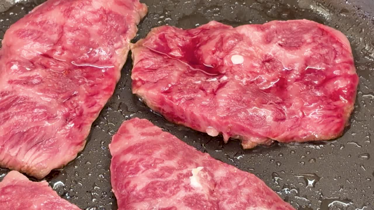 Primo piano di bistecche di manzo marmorizzate roventi che sfrigolano in una padella calda