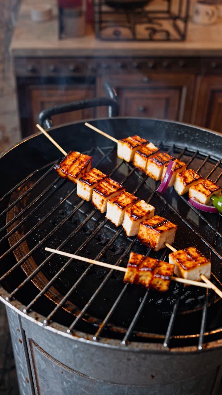 Top-down video shot of grilled skewers with tofu and vegetables on a barbecue, capturing smoky