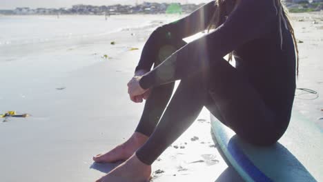 video de un hombre caucásico sonriente con rastas en traje de neopreno sentado en una tabla de surf en una playa soleada