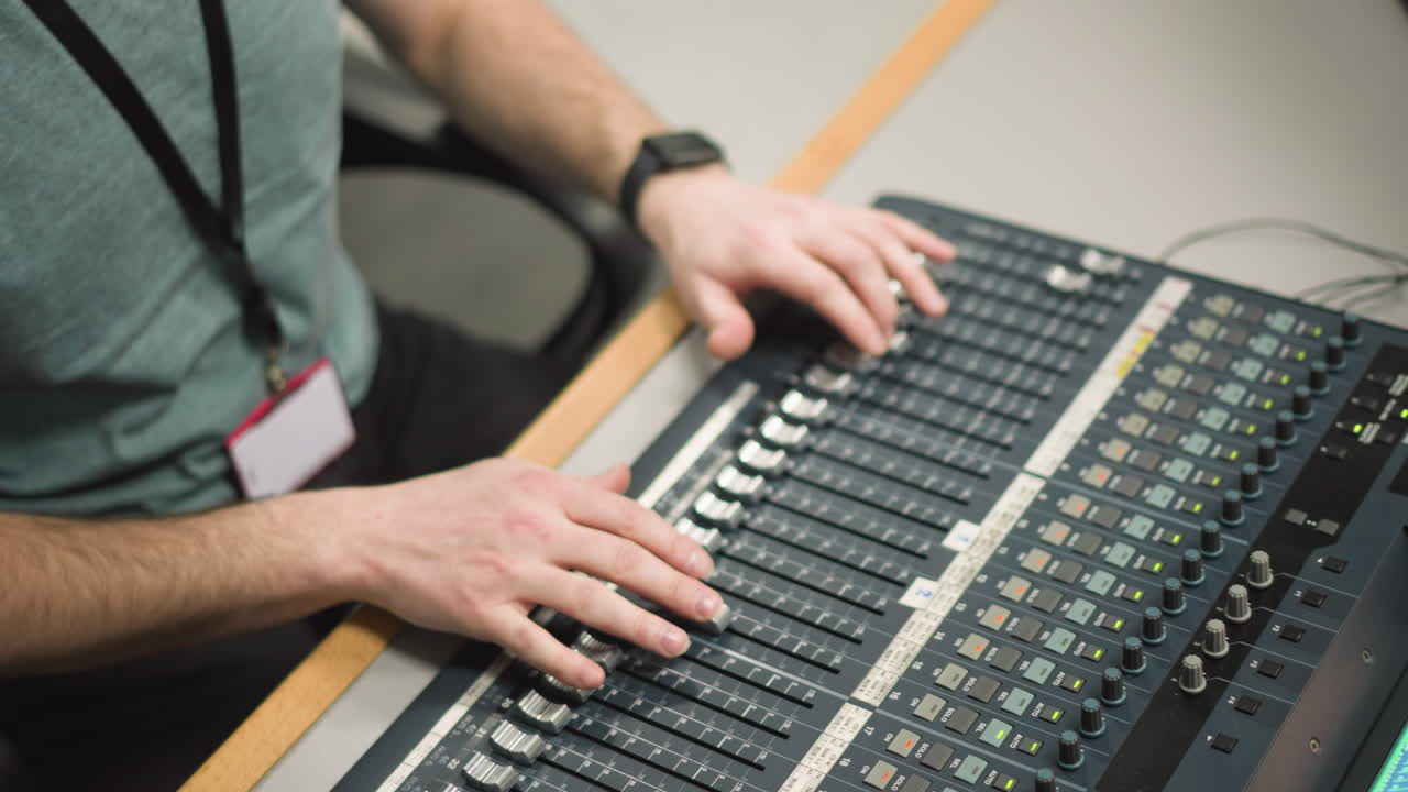Close-up of hands adjusting audio faders on broadcast sound mixing desk. Professional sound engineer operating mixing console with multiple channels in broadcast studio during media production