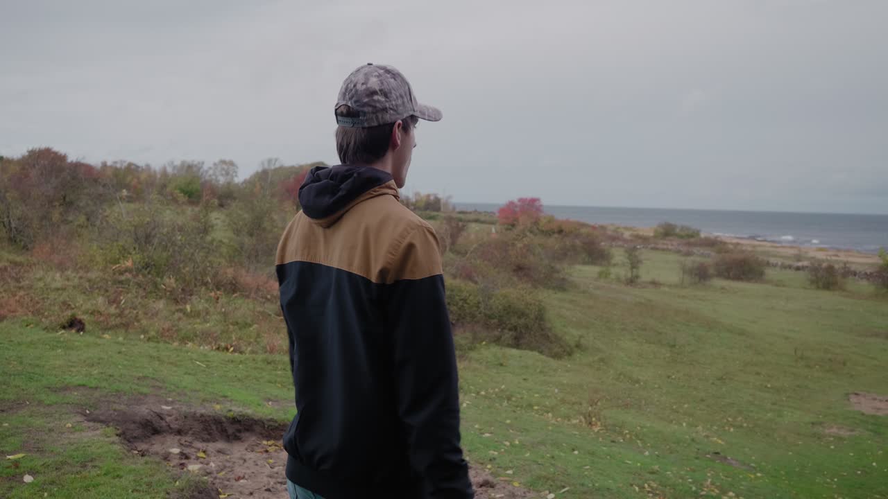 모자를 쓴 스칸디나비아의 젊은 키 큰 남자가 멈춰서 simrishamn sweden österlen의 vårhallarna를 바라본다 - 추적 중간 샷