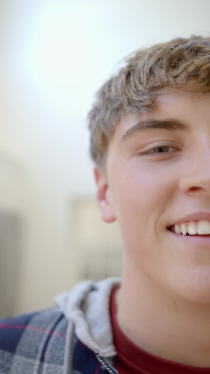 Vertical video of portrait of happy caucasian male teenager with blond hair at home, slow motion