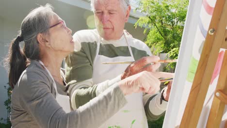 happy diverse senior couple painting in garden on sunny day