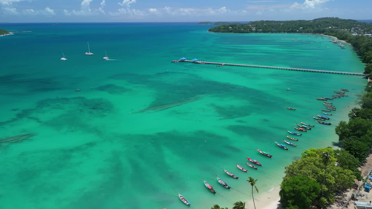Drone flies right then pans left above Rawai Beach, pier and longtail boats