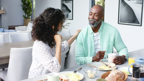 Happy-biracial-couple-having-scrambled-eggs-for-breakfast-and-talking-in-kitchen,-slow-motion