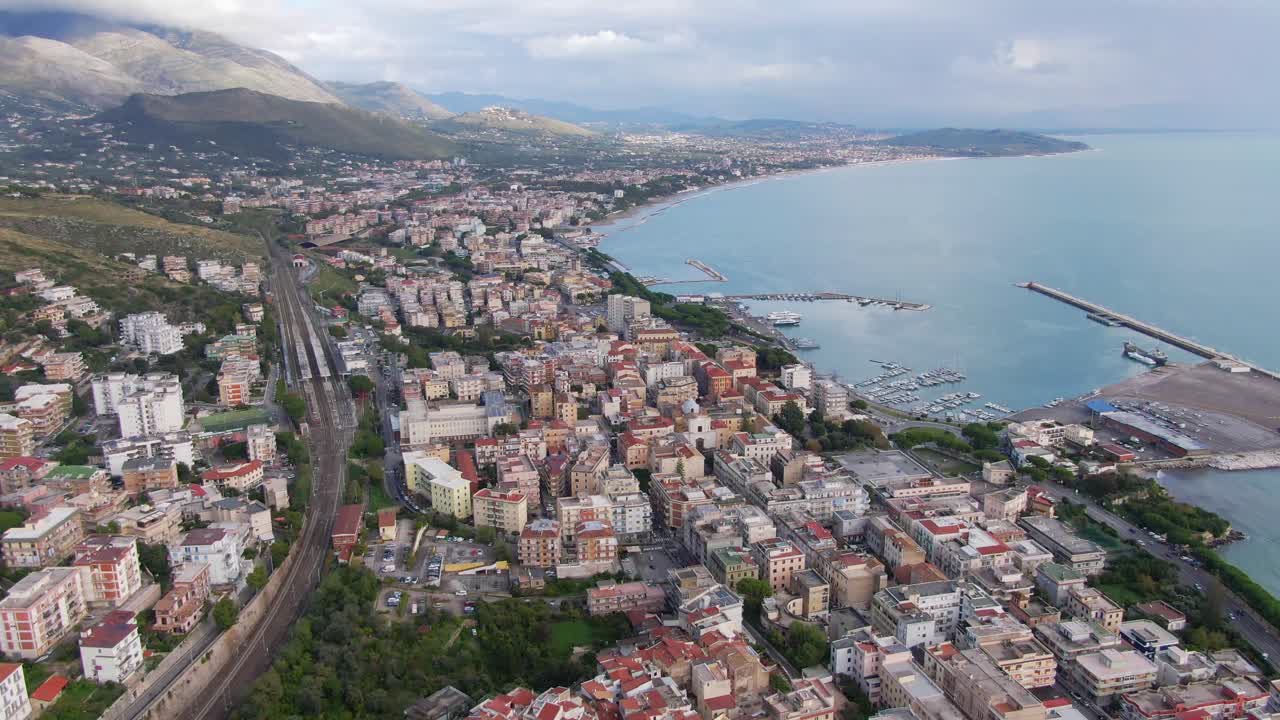 Aerial view of seaside downtown urban Gaeta city buildings with view of seaport marina and mountain range in background, Italy, drone