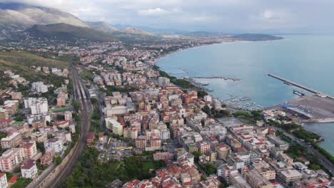 aerial view of seaside downtown urban gaeta city buildings with view of seaport marina and mountain range in background, italy, drone