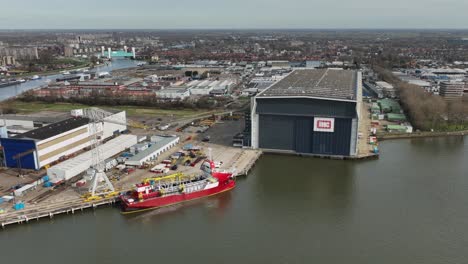 large red transport boat offloading cargo at warehouse, rotterdan, holland, aerial wide angle shot