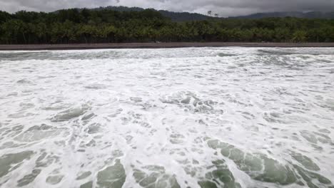 Aerial-Dolly-Im-Türkisfarbenen-Schäumenden-Meer-In-Der-Nähe-Der-Küste-Mit-Dschungel-Im-Hintergrund-In-Dominicalito-Beach,-Costa-Rica