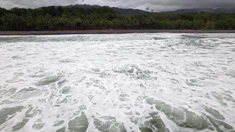 aerial dolly in of turquoise foamy sea near the shoreline with jungle in background in dominicalito beach, costa rica