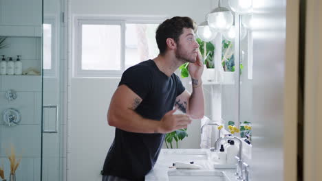 man wearing pyjamas standing at sink putting on moisturizer in bathroom