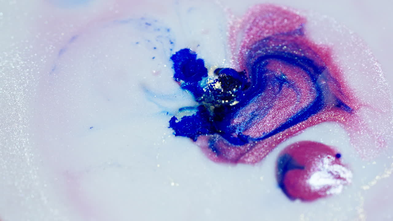 Vibrant blue and pink inks spreading in water with a glittery effect, close-up