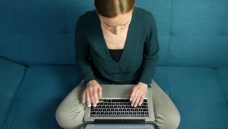 top view of a woman working on a laptop sitting on a sofa