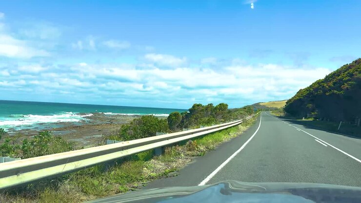 A car journey along the Great Ocean Road, capturing coastal views and lush greenery under bright daylight