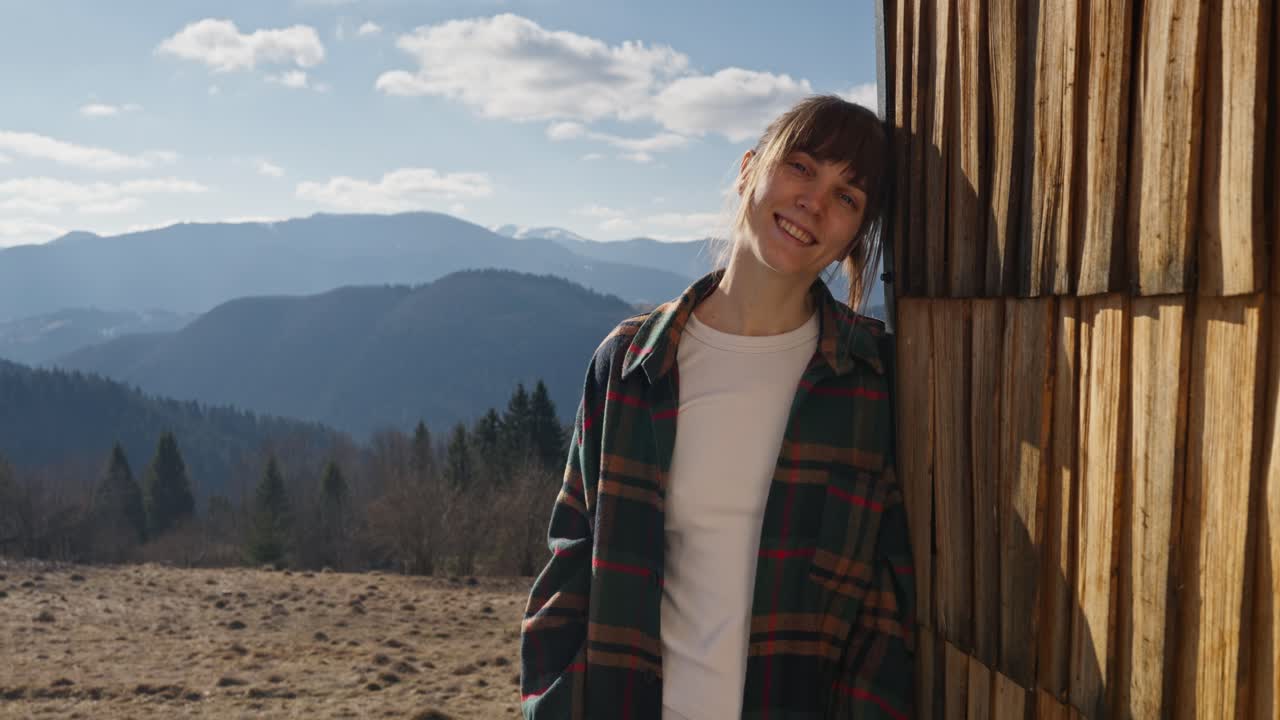 Woman in plaid shirt leaning against a cabin in the mountains
