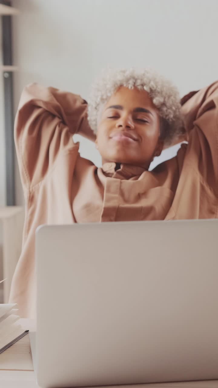 Young african american woman puts hands behind head and leans back in chair