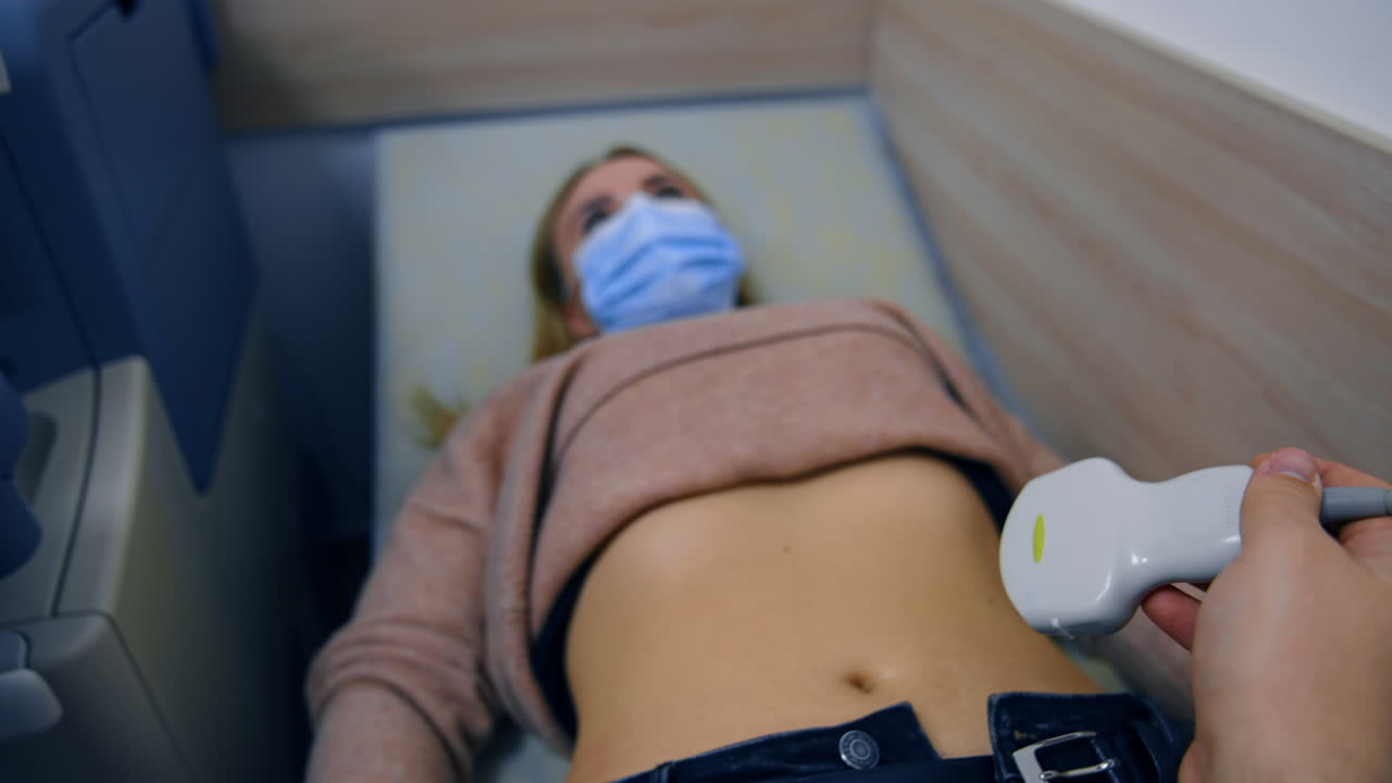 Male hand holding the ultrasound transducer device approaches the patient. Ultrasonic check up of inner organs.