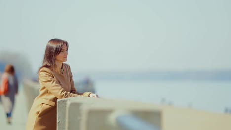 young brunette woman stands at the parapet and looks thoughtfully into the distance. spring walk along the promenade. circular motion of the camera.