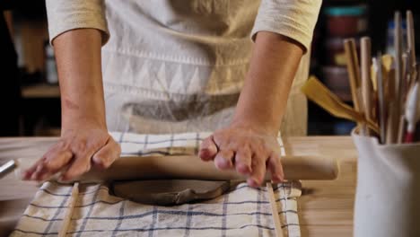 young woman potter rolling out a piece of clay using a rolling pin