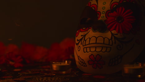 still life of decorated skull mask next to smouldering blown out candle and flowers celebrating mexican holiday of dia de muertos or day of the dead against dark background