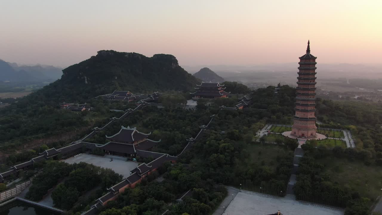 vista aérea de drones en vietnam volando lejos de un templo budista y área de pagoda en ninh binh al atardecer rodeado de montañas verdes