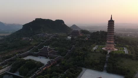 drone aerial view in vietnam flying away from a buddhist temple and pagoda area in ninh binh at sunset surrounded by green mountains