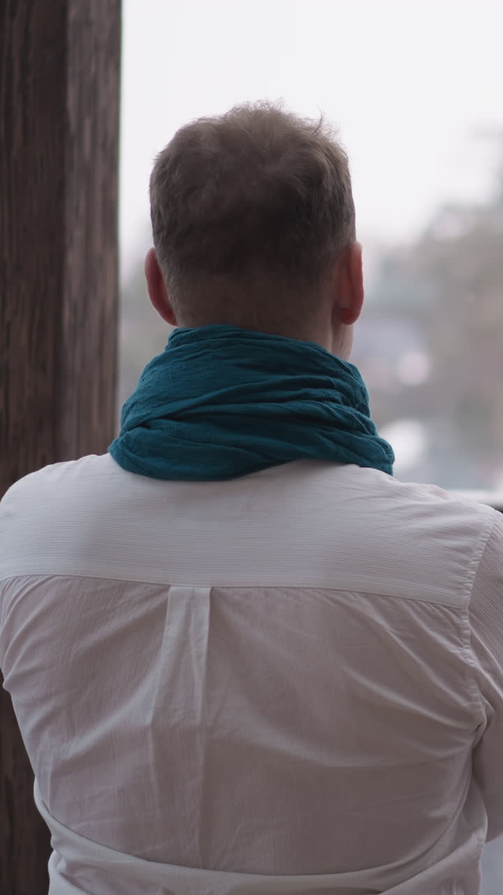 사람은 창문으로 겨울의 그림을 흡수합니다. 집중된 사람은 집의 평화로운 고립에서 문제를 해결하는 것에 대해 생각하고 있습니다. 평온한 고독.