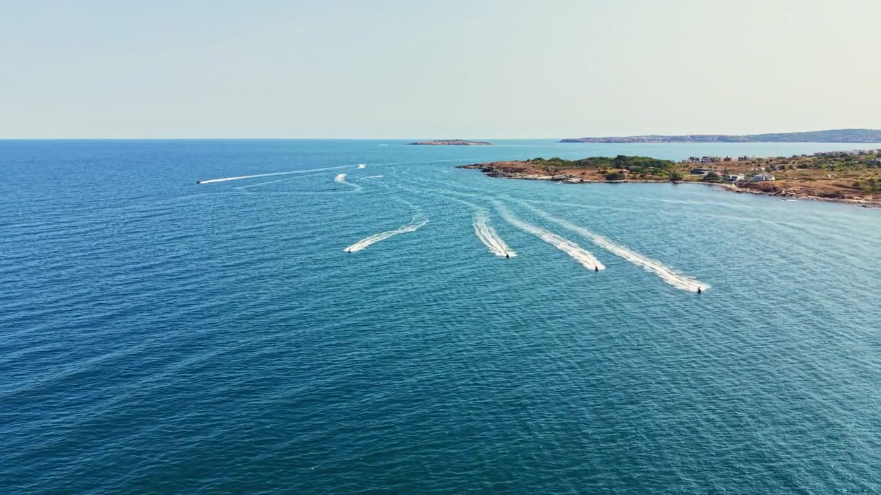 Barche che si muovono nell'acqua vicino a una costa con terra verde sullo sfondo in una giornata di sole